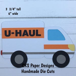 May include: A white die-cut U-Haul truck with orange and black lettering, a blue window, and black wheels. The truck is 3 3/4 inches tall and 6 inches wide. The text "CKS Paper Designs Handmade Die Cuts" is at the bottom.