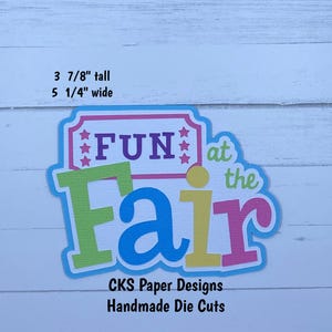 May include: A colorful die-cut paper design with the words "FUN at the Fair." The design is approximately 3 7/8 inches tall and 5 1/4 inches wide. The text is in various colors, including green, blue, purple, pink, and yellow. The design also includes the text "CKS Paper Designs Handmade Die Cuts."