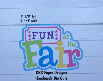 May include: A colorful die-cut paper design with the words "FUN at the Fair." The design is approximately 3 7/8 inches tall and 5 1/4 inches wide. The text is in various colors, including green, blue, purple, pink, and yellow. The design also includes the text "CKS Paper Designs Handmade Die Cuts."