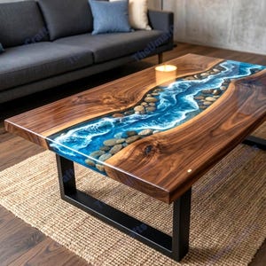 Könnte beinhalten: Rechteckiger Couchtisch mit Flussdesign. Der Tisch hat einen dunklen Holzrahmen mit einem blauen Harzmittelteil, das Wasser und Steine simuliert. Er hat schwarze Metallbeine und steht auf einem gewebten Teppich.