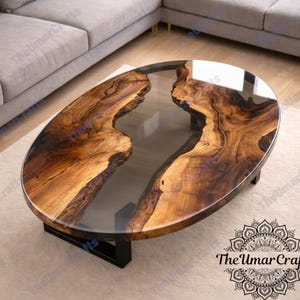 Könnte beinhalten: Ovaler Couchtisch mit einer Baumkante und einem transparenten Epoxidharz-Mittelteil. Der Tisch hat ein dunkelbraunes und beiges Holzmaserungsmuster und steht auf einem schwarzen Sockel. Der Tisch ist etwa 122 cm lang.