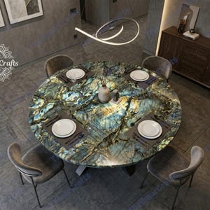 May include: A round dining table with a unique, multi-colored stone top, set for four. The table features a mix of blue, green, and gold hues. Each place setting includes a white plate, silverware, and a dark gray placemat. Four gray chairs surround the table.