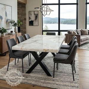 Może przedstawiać: Prostokątny stół jadalniany z polerowanym blatem z białego marmuru i czarną metalową podstawą w kształcie litery X, otoczony sześcioma ciemnoszarymi tapicerowanymi krzesłami na cienkich czarnych metalowych nogach. Stół stoi na szaro-białym dywanie.