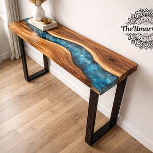 May include: A rectangular console table featuring a natural wood slab with a live edge and a central blue epoxy resin river inlay. The table is supported by two black metal U-shaped legs. The text The Umar Crafts is visible in the upper right.