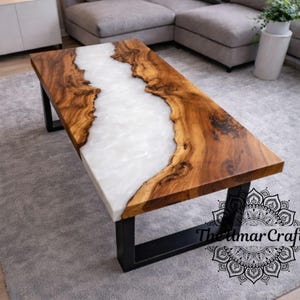 May include: A rectangular coffee table with a live edge wood top and a white resin river. The table is supported by black metal legs. The table measures approximately 48 inches long, 24 inches wide, and 16 inches high.
