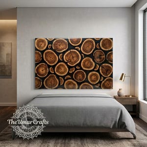May include: A rectangular wall art piece featuring a mosaic of circular wood slices with visible grain patterns and dark brown bark edges, set against a black background. The artwork is displayed above a grey bed with a white logo in the corner.