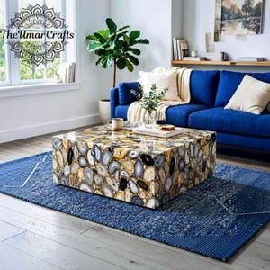 May include: A square coffee table featuring a mosaic surface composed of numerous polished agate slices in shades of gray, white, brown, and black. The table has a smooth, reflective finish and a boxy, low-profile design with clean, straight edges.