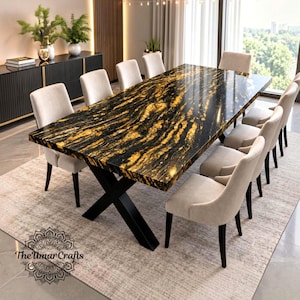 Op de afbeelding: Een rechthoekige eettafel met een gepolijst zwart en goud marmeren blad en een zwart metalen X-vormig onderstel, omringd door acht gestoffeerde beige stoelen. Het logo The Umar Crafts is zichtbaar in de linkerbenedenhoek van de afbeelding.