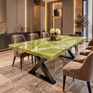May include: A rectangular dining table with a polished green onyx stone top featuring white veining and a black metal X-shaped base. The table is surrounded by six upholstered taupe chairs with dark legs, arranged on a textured area rug.