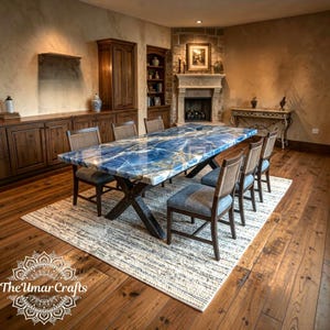 Puede incluir: Una mesa de comedor rectangular con un tablero de piedra azul pulida con vetas blancas y una base de madera oscura en forma de X. Seis sillas con estructura de madera oscura, respaldo de rejilla y asiento gris están dispuestas alrededor.