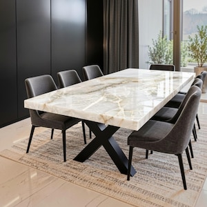 May include: A rectangular dining table with a polished white and cream marble top featuring prominent veining, supported by a black metal X-shaped base. The table is surrounded by six upholstered charcoal grey dining chairs with black legs.