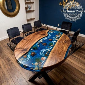 May include: An oval dining table featuring a natural wood grain surface with a central river design made of blue resin. The resin inlay contains embedded sea shells, small turtle figurines, and green aquatic plants. The table has a dark base.