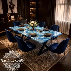 Puede incluir: Una mesa de comedor rectangular con tablero de resina veteada en azul y blanco y base de metal negro en forma de X, rodeada de seis sillas tapizadas en terciopelo azul marino con patas de metal dorado, servida con platos negros.