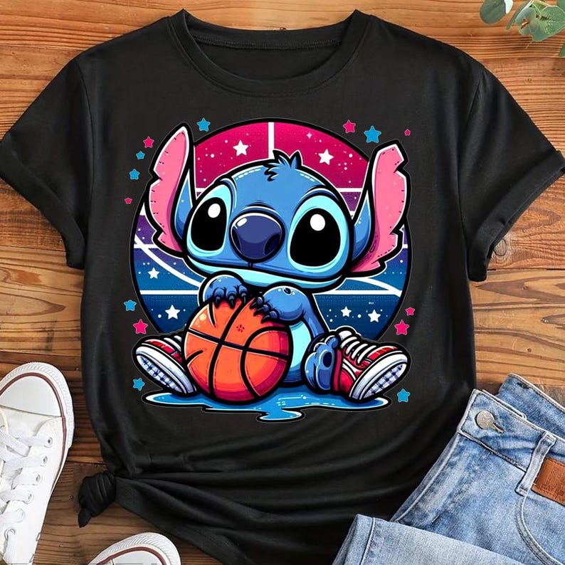 May include: Black t-shirt featuring a cartoon character holding a basketball. The character is blue with large eyes and pink ears, set against a pink and blue background with stars. The basketball is orange and brown. The character is wearing red and white sneakers.