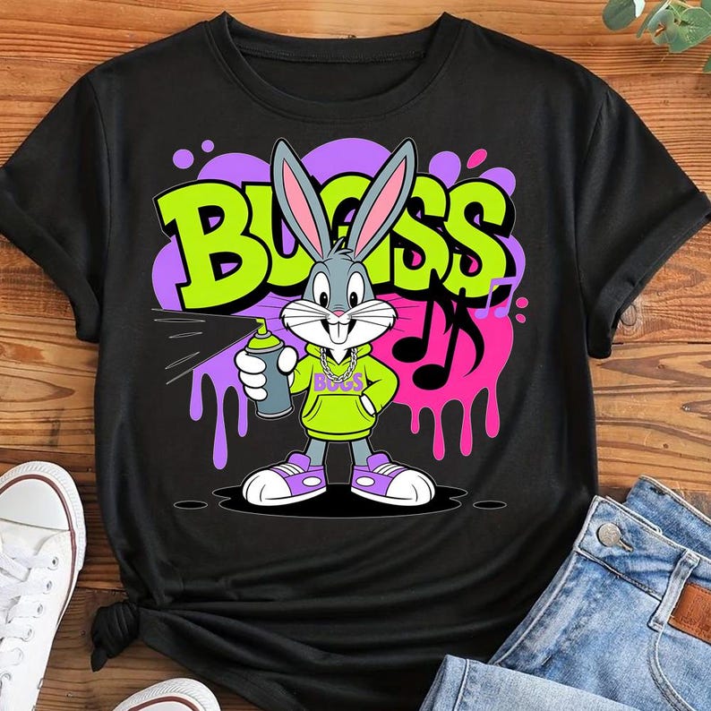 May include: Black t-shirt featuring Bugs Bunny holding a spray can, with the word "BLISS" in a graffiti-style design. The cartoon character is wearing a green hoodie and purple sneakers. Musical notes and paint drips add to the urban art theme.
