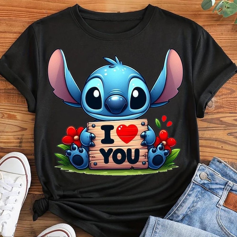 May include: Black t-shirt featuring a blue cartoon character holding a wooden sign with "I ❤️ YOU" written on it. The character has large ears and big eyes. Red flowers and green grass are also in the design.