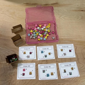 May include: A pink plastic container filled with colorful miniature figurines, including butterflies, bears, and flowers. Several small cardboard boxes and six cards with the text "Order #" and numbered illustrations are also present.
