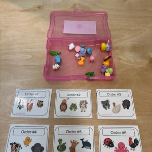 May include: A translucent pink plastic storage container holding various small, colorful animal figurines. Below the container are six white square cards labeled Order #1 through Order #6, each featuring three distinct cartoon animal illustrations.
