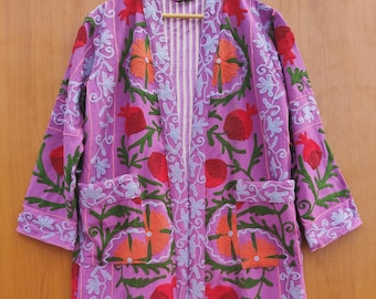 May include: A long, open-front robe in a vibrant purple hue, adorned with intricate floral embroidery. The design features red, orange, and green flowers and foliage. The robe has two pockets and is approximately 55 inches long.