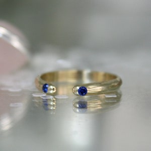 May include: A gold ring with two small blue gemstones set into the band.