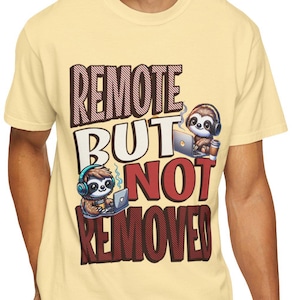 Könnte beinhalten: Ein hellgelbes T-Shirt mit dem Text "REMOTE BUT NOT REMOVED" in Burgunderrot und Weiß. Das Design zeigt Cartoon-Faultiere mit Kopfhörern und Laptops. Die Person trägt eine blaue Jeans.