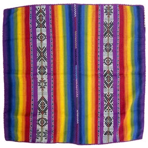 Puede incluir: Un tejido rectangular con rayas verticales en tonos vibrantes de morado, rojo, naranja, amarillo, verde y azul. La tela incluye dos bandas blancas distintas decoradas con intrincados patrones geométricos de diamantes en negro y rojo.