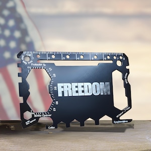 May include: Black multi-tool card with the word "FREEDOM" in silver. The card has various cut-out tools, including a bottle opener, cutter, and ruler with centimeter markings. An American flag is in the background.