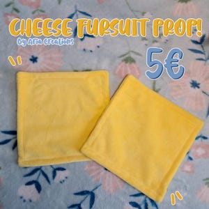 Puede incluir: Dos accesorios cuadrados amarillos para fursuit, que simulan rebanadas de queso. Los accesorios están hechos de un material suave y afelpado con un borde cosido. El texto en la imagen dice "CHEESE FURSUT PROP!" y "By Aria Creations".
