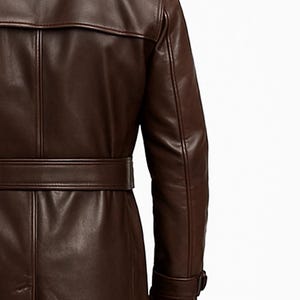May include: A brown leather trench coat with a belted waist and a notched collar. The coat features a classic design with a buttoned cuff and a back vent. The leather appears smooth and has a slight sheen.