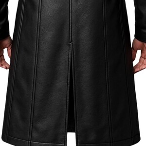 May include: A long black coat featuring a textured surface and vertical seam detailing. The garment includes a central back vent that extends upward from the hem, creating a structured silhouette with clean lines and a consistent matte black finish.
