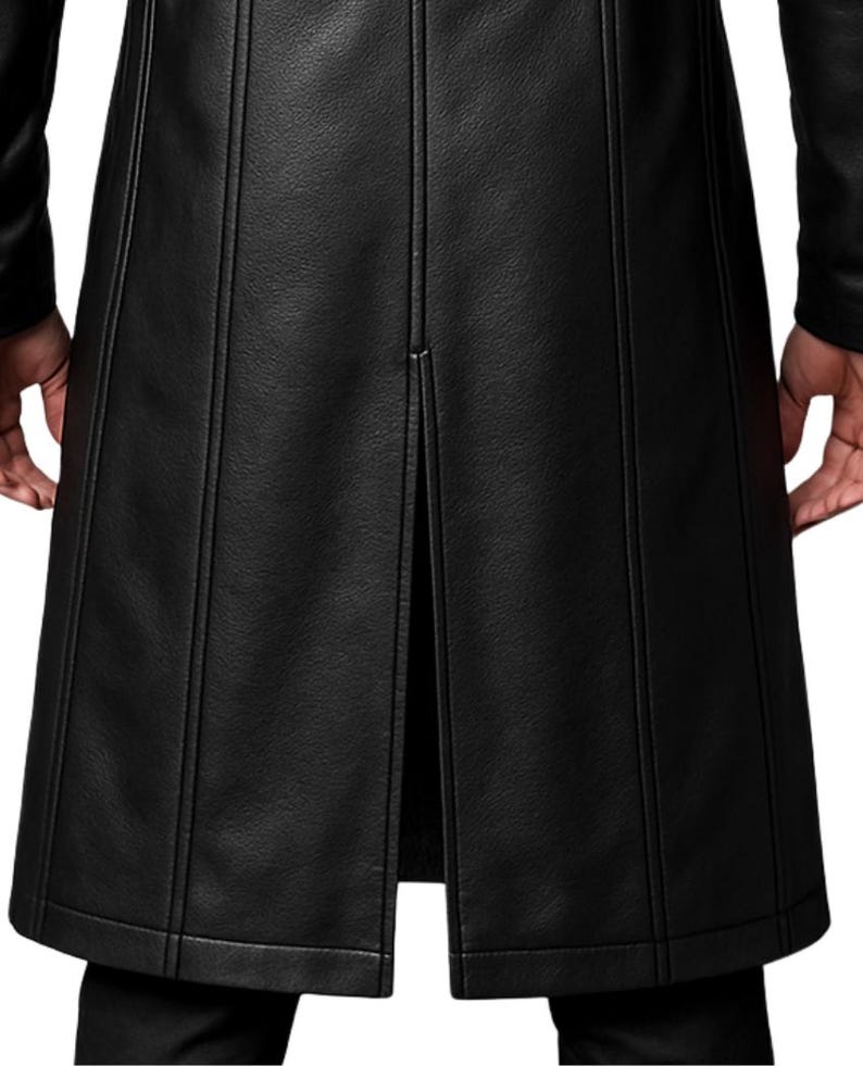 May include: A long black coat featuring a textured surface and vertical seam detailing. The garment includes a central back vent that extends upward from the hem, creating a structured silhouette with clean lines and a consistent matte black finish.