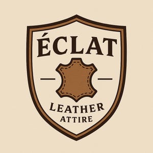 May include: A brown and beige shield-shaped logo with the text "&Eacute;CLAT" at the top and "LEATHER ATTIRE" at the bottom. A brown leather patch is in the center. The logo has a vintage aesthetic.