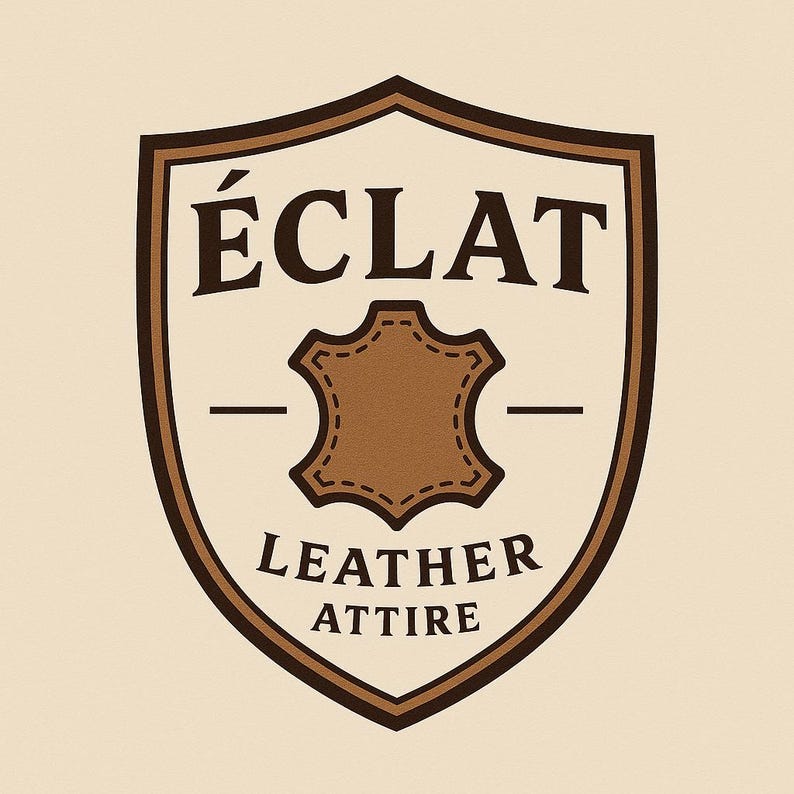 May include: A brown and beige shield-shaped logo with the text "&Eacute;CLAT" at the top and "LEATHER ATTIRE" at the bottom. A brown leather patch is in the center. The logo has a vintage aesthetic.