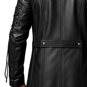 May include: A black leather jacket featuring vertical seam detailing, a horizontal waist strap with two silver-toned metal snaps, and a sleeve design with a buckled strap and multiple silver-toned studs along the outer arm.