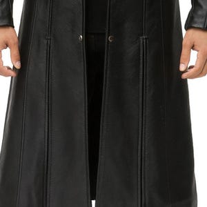 May include: A long black coat featuring a smooth texture, vertical seam detailing, and a front opening with visible metal snap buttons. The garment extends past the waist, showcasing a structured design with long sleeves and a clean, minimalist finish.