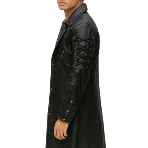 May include: A black long coat featuring a structured collar and a front button closure. The sleeves are detailed with black lace-up cord accents through metal eyelets, complemented by a series of silver-toned metal studs along the forearm area.