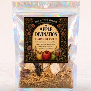 May include: A holographic pouch containing a botanical simmer blend labeled The Witch's Kitchen Apple Divination. The label features illustrations of apples and flowers, listing ingredients including apple, yarrow, red clover, cardamom, vanilla, and Egyptian geranium.