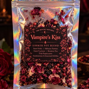 Puede incluir: Una bolsa holográfica que contiene una mezcla para olla a fuego lento etiquetada como Vampire's Kiss. La etiqueta enumera ingredientes como pétalos de rosa, flores de hibisco, pasas de Corinto, té Keemun, pimienta rosa e incienso.