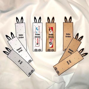 Può includere: Segnalibri a tema pasquale con orecchie da coniglio. Alcuni hanno il testo "Suße Grüße", "Hasen Gruß" e "Für Dich". Altri presentano confezioni di cioccolato Kinder e il testo "Frohe Ostern".
