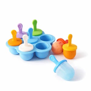 Könnte beinhalten: Eine blaue Eis am Stiel-Form mit sechs Vertiefungen, jede mit einem unterschiedlich farbigen Deckel: orange, lila, grün, weiß und blau. Mehrere gefüllte und ungefüllte Eis am Stiel liegen neben der Form. Die Eis am Stiel haben gelbe, orangefarbene und rote Deckel.