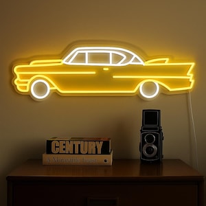 Puede incluir: Un letrero de neón amarillo con la forma de un coche clásico está montado en una pared. El contorno del coche brilla, con detalles blancos. Debajo, un mueble de madera oscura exhibe una cámara vintage y libros, incluido uno titulado "CENTURY".
