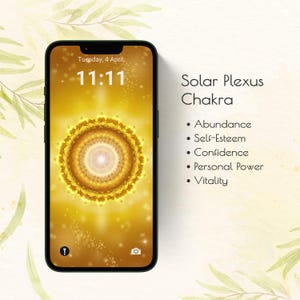 Puede incluir: Un smartphone muestra un diseño de chakra del plexo solar de color amarillo dorado. La pantalla muestra la hora 11:11 y la fecha. El texto de la derecha enumera los atributos: Abundancia, Autoestima, Confianza, Poder personal y Vitalidad.