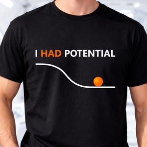 Pode incluir: T-shirt preto com o texto "I HAD POTENTIAL" em branco e laranja. O design inclui uma linha branca e uma bola laranja. A camisa é de estilo gola redonda clássica.