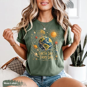 Puede incluir: Camiseta verde musgo con un gr&aacute;fico de la Tierra rodeada de planetas y un sol, con el texto "Earth Day Every Day" en blanco. La camiseta est&aacute; hecha de un material suave.