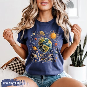 Puede incluir: Camiseta azul marino con un dise&ntilde;o del D&iacute;a de la Tierra. El dise&ntilde;o presenta la Tierra rodeada de planetas, un sol y el texto "Earth Day Every Day". La camiseta es de color azul marino.