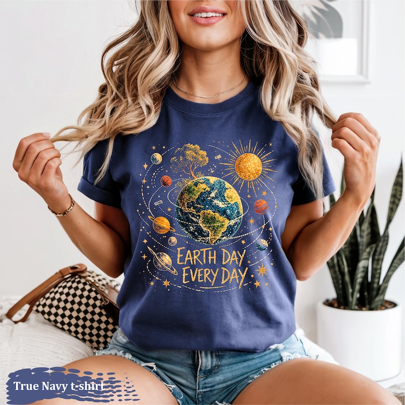 Puede incluir: Camiseta azul marino con un dise&ntilde;o del D&iacute;a de la Tierra. El dise&ntilde;o presenta la Tierra rodeada de planetas, un sol y el texto "Earth Day Every Day". La camiseta es de color azul marino.