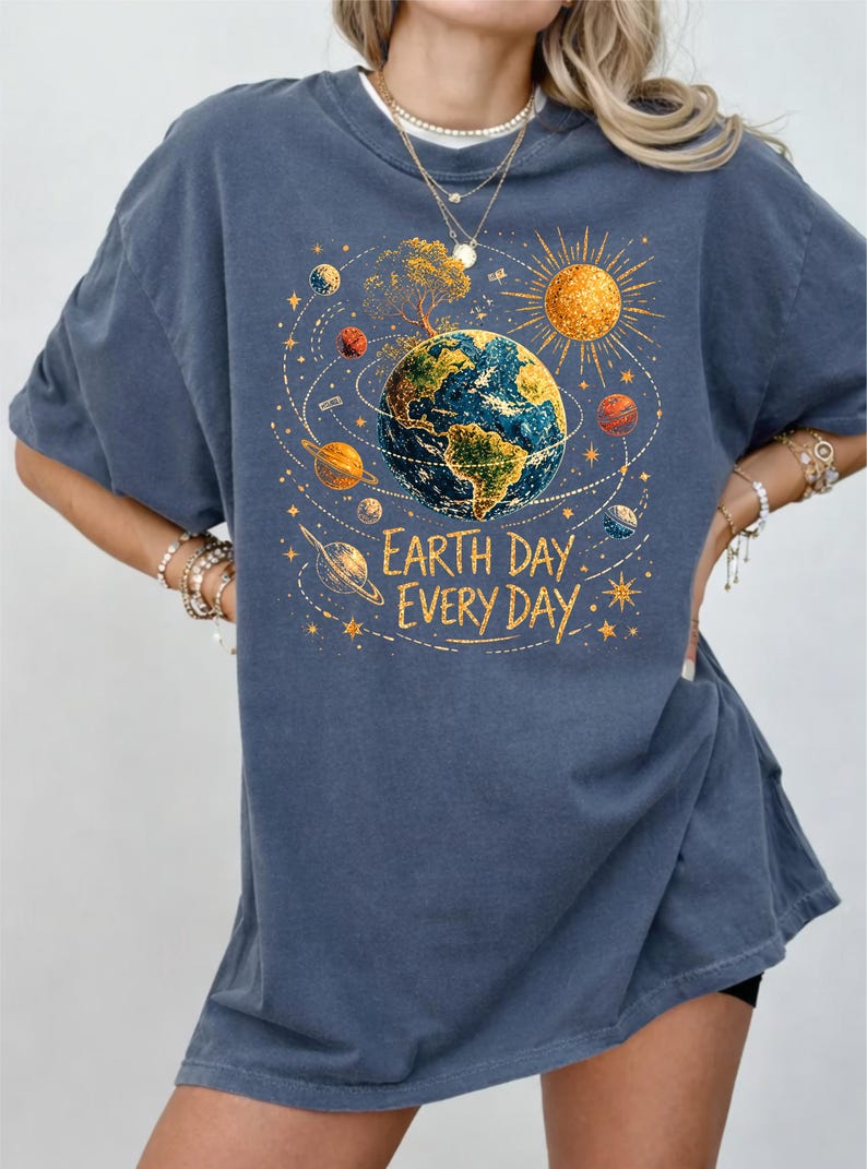 Puede incluir: Camiseta azul con un gr&aacute;fico colorido de la Tierra rodeada de planetas, un sol y un &aacute;rbol. El texto "Earth Day Every Day" est&aacute; impreso debajo. La camiseta tiene mangas cortas y cuello redondo.