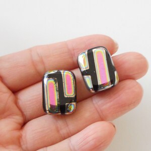 May include: A pair of iridescent black and pink glass earrings with a geometric pattern. The earrings are rectangular in shape and have a shiny finish.