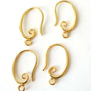 May include: Four gold-colored earring hooks. Each hook has a curved design with a looped bottom for attaching charms and a decorative swirl at the top. The hooks are displayed against a white background.