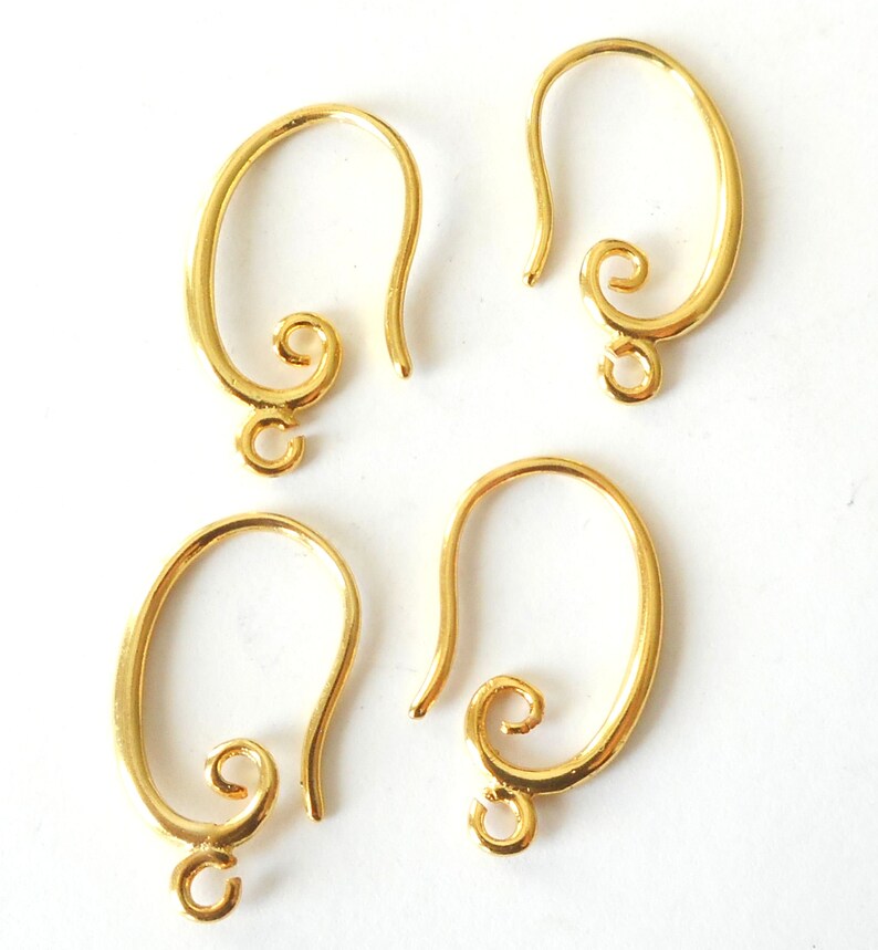 May include: Four gold-colored earring hooks. Each hook has a curved design with a looped bottom for attaching charms and a decorative swirl at the top. The hooks are displayed against a white background.